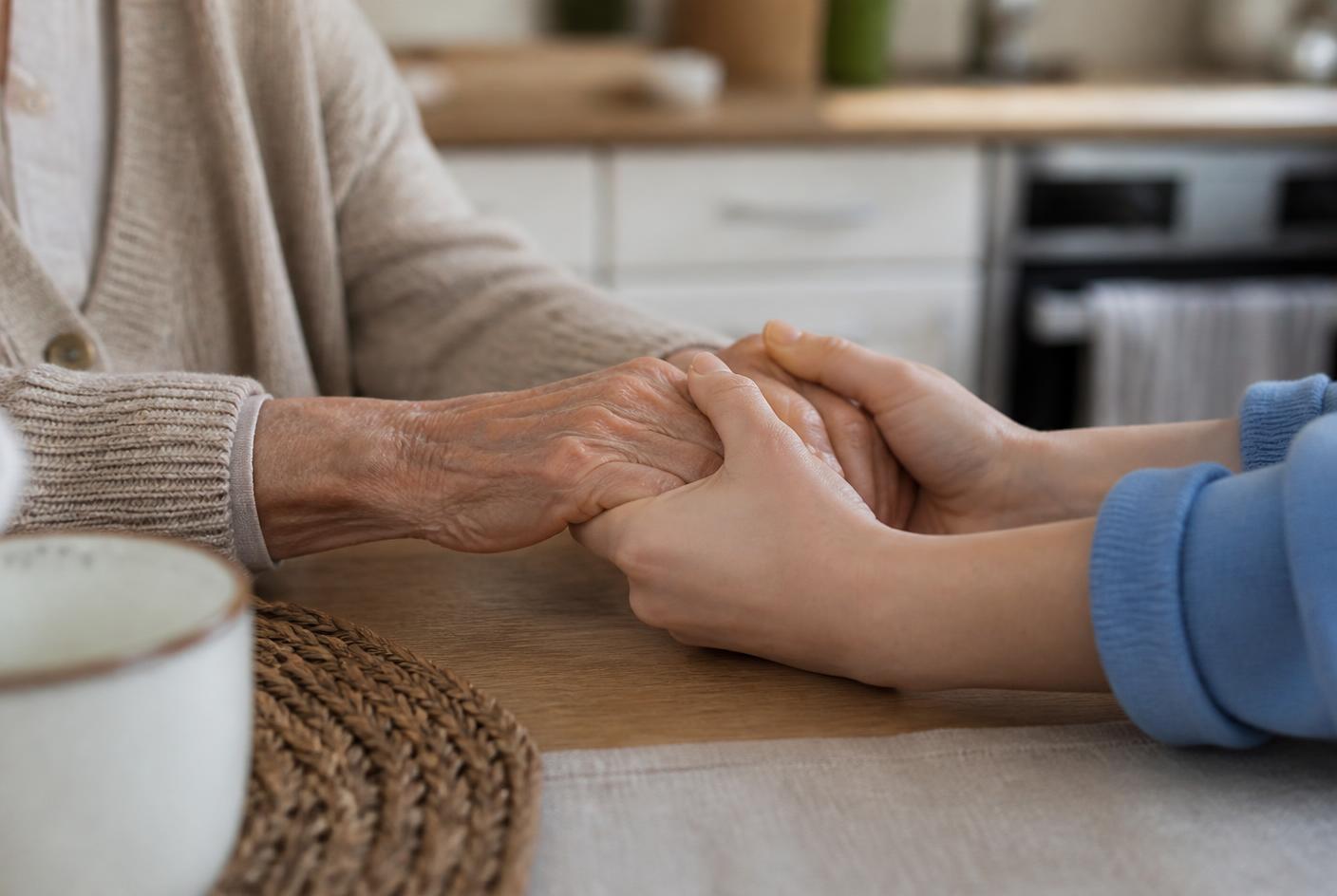 A caregiver holding the hands of an older adult across a kitchen table